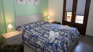 Un dormitorio con cama, dos mesitas de noche, una mesita auxiliar, una ventana con persianas y una puerta.