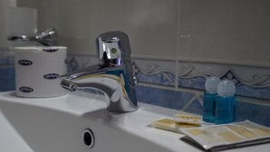 Un lavamanos con grifo cromado, dispensador de papel higiénico y dos botellas de jabón azul.