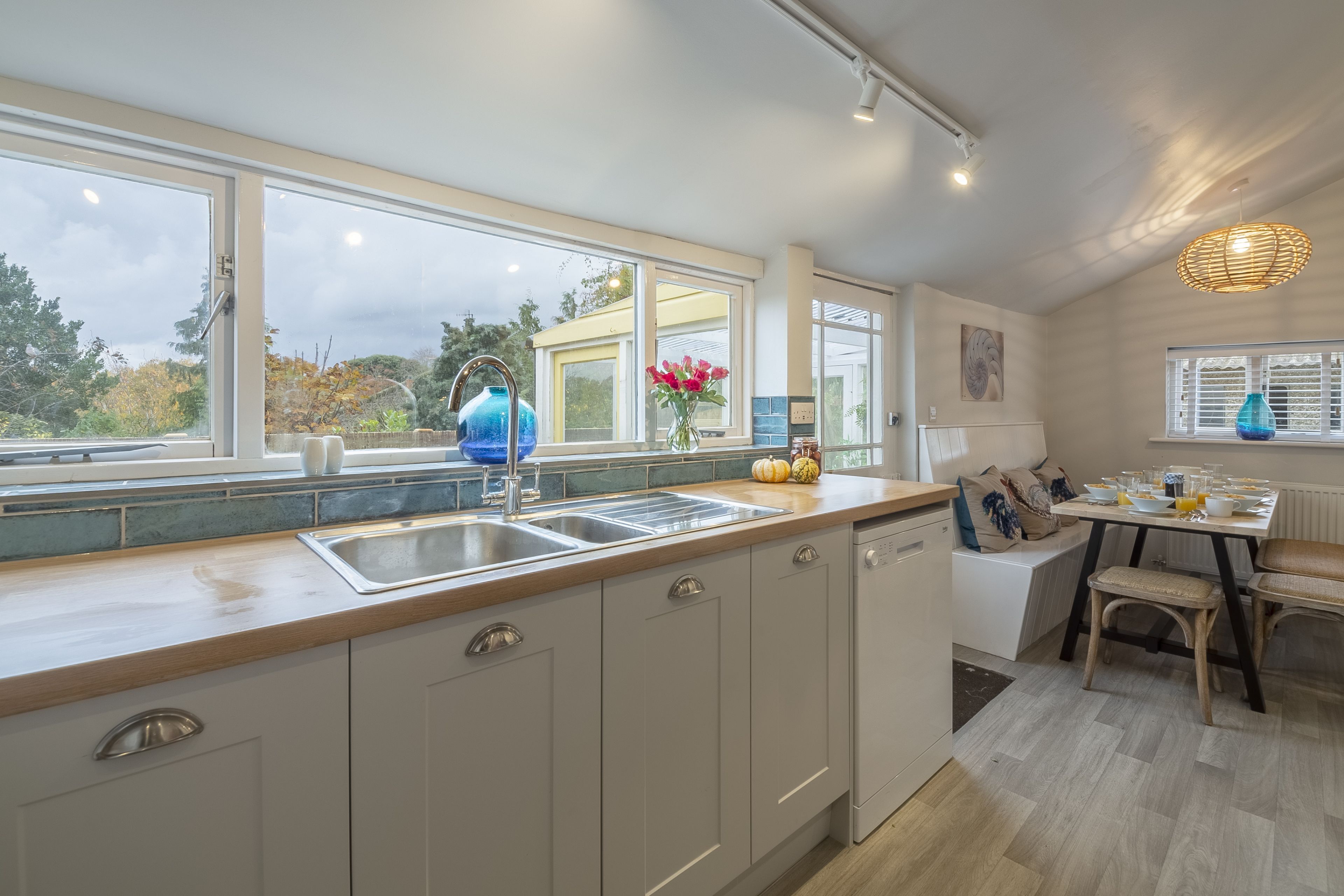 A modern kitchen with a large window, a sink, and a dining area with a table and chairs.