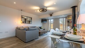 A modern living room with a grey sofa, dining table with chairs, and a TV. - Wheelwrights, Sustead, Norfolk (Sustead)