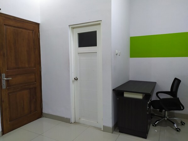 A room with a wooden door, a white door with a window, a black desk with a black office chair, and a green accent wall. - Green Belt Kost Exclusive (Ngemplak)