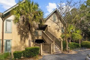 A two-story building with a wooden exterior, a staircase, and a palm tree in the foreground.