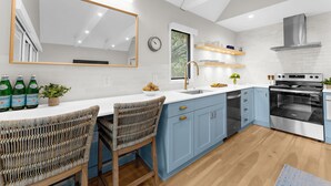 A modern kitchen with blue cabinets, a large mirror, a built-in oven, and a dining area with wicker chairs.