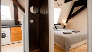 A compact kitchen with a washing machine, a wooden cabinet, and a dark wooden door. - Sunny mansard in the heart of Old Town (Centra rajons)
