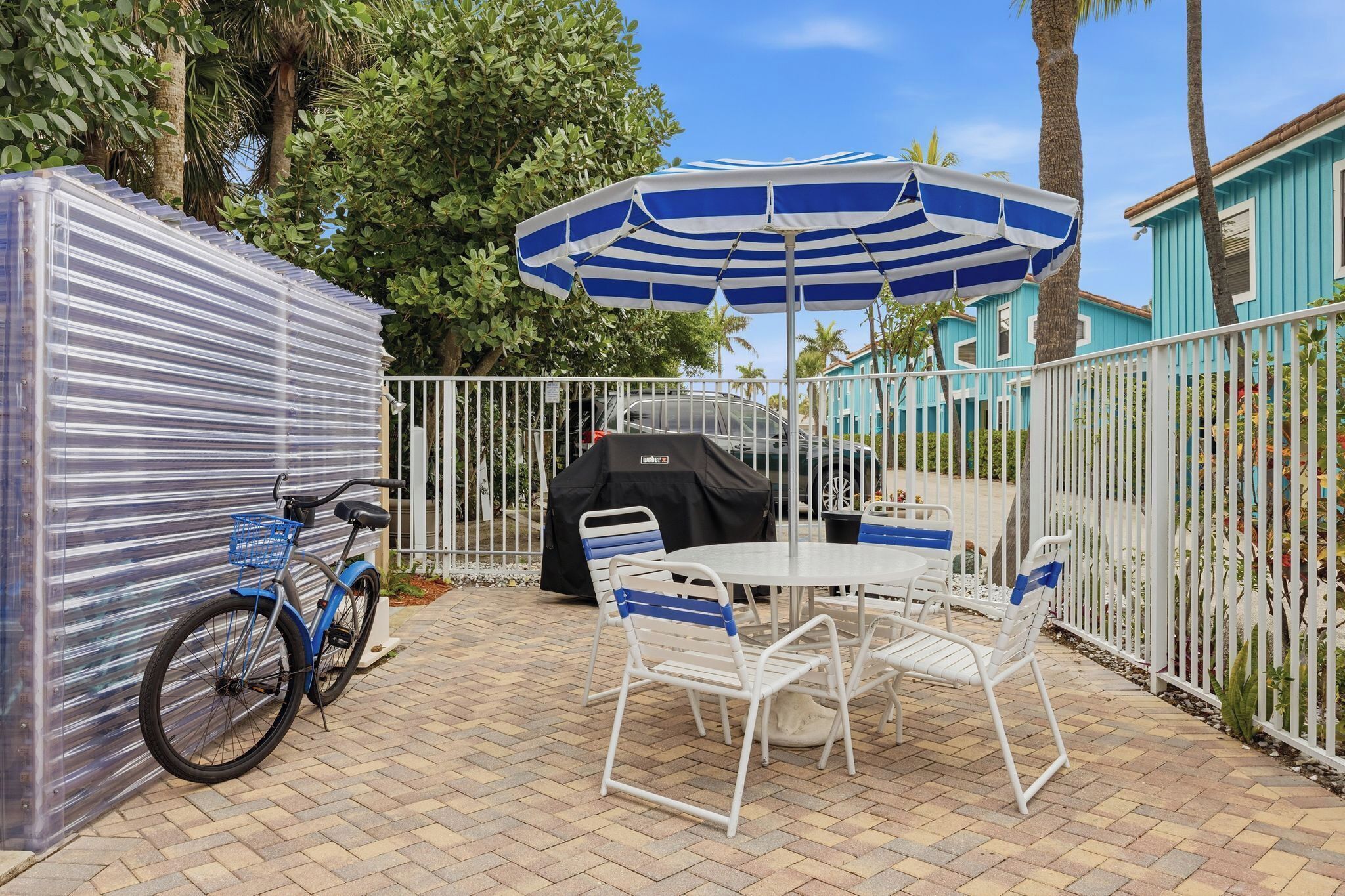 A patio area with a table and chairs, a blue and white striped umbrella, a covered grill, and a bicycle.