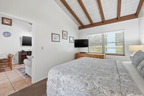 A bedroom with a large bed, a desk with a chair, a television, and a window with blinds. - Sand Dune Shores (Singer Island)