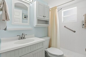 A bathroom with a white sink, vanity, and toilet. There is a shower with a glass door and a handrail. - Sand Dune Shores (Singer Island)