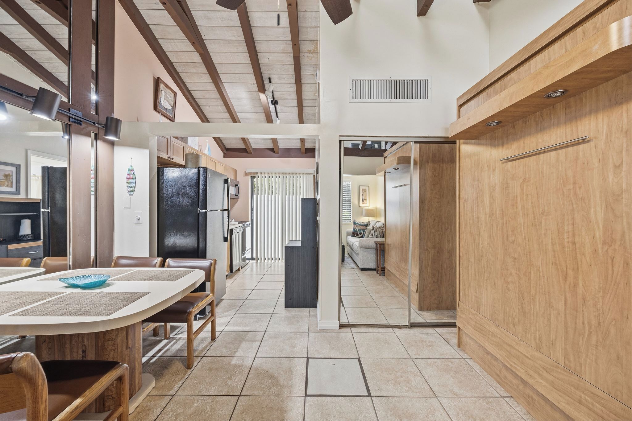 Una cocina moderna con vigas de madera, un comedor con una mesa grande y sillas, y vistas a una sala de estar con un sofá y una ventana.