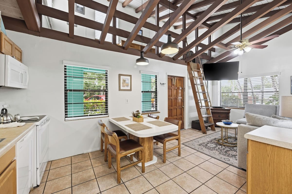 A spacious kitchen with a dining area, wooden beams, white cabinets, and a tiled floor.