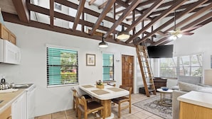A spacious kitchen with a dining area, wooden beams, white cabinets, and a tiled floor.