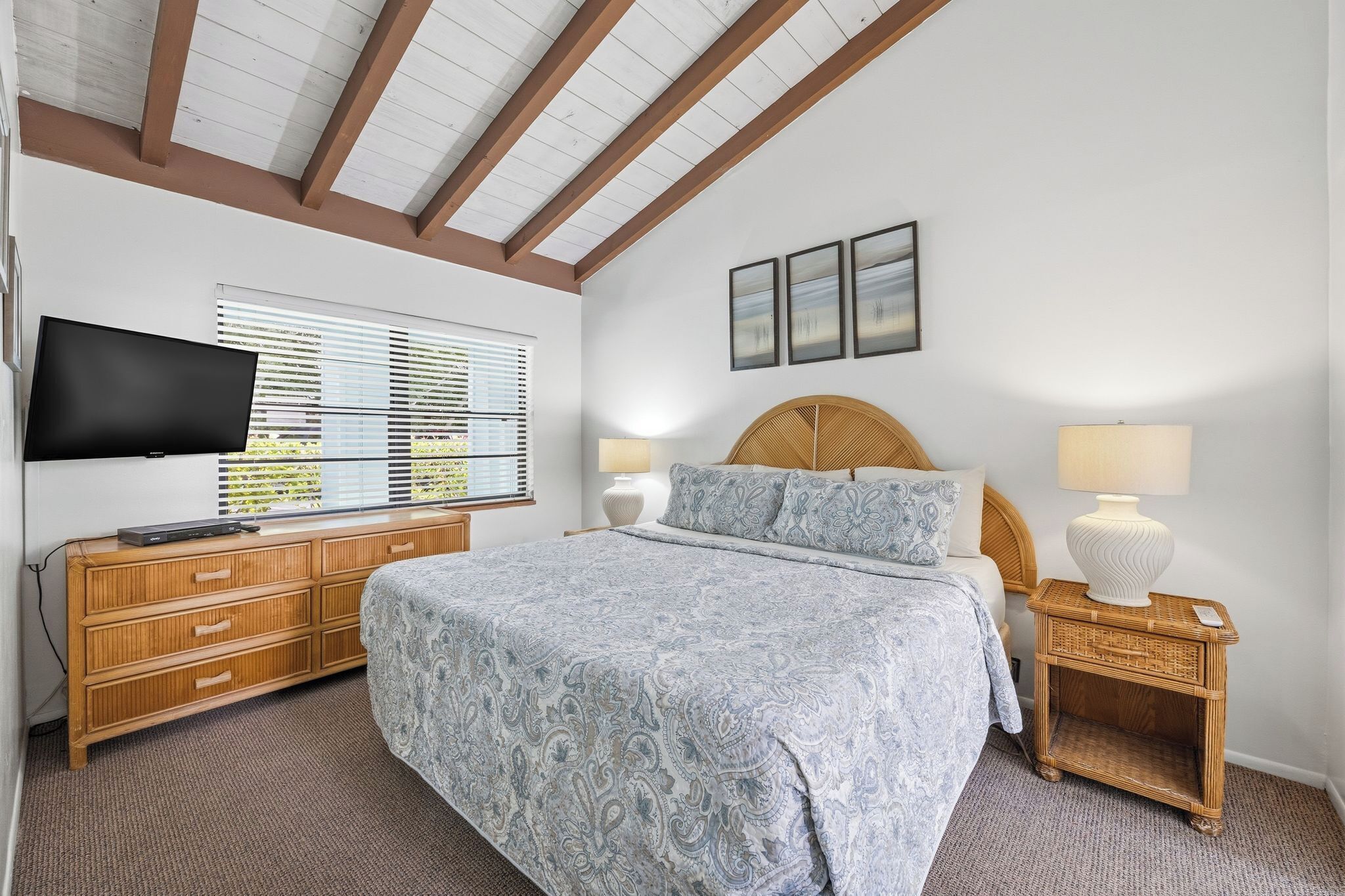 A bedroom with a bed, a TV, a bedside table with a lamp, and a window with blinds.