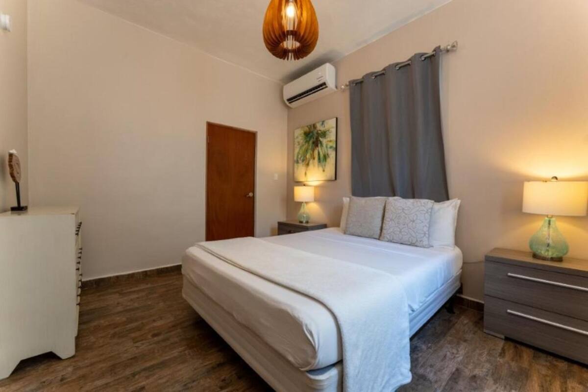 A bedroom with a bed, bedside tables, a lamp, an air conditioner, and a door.