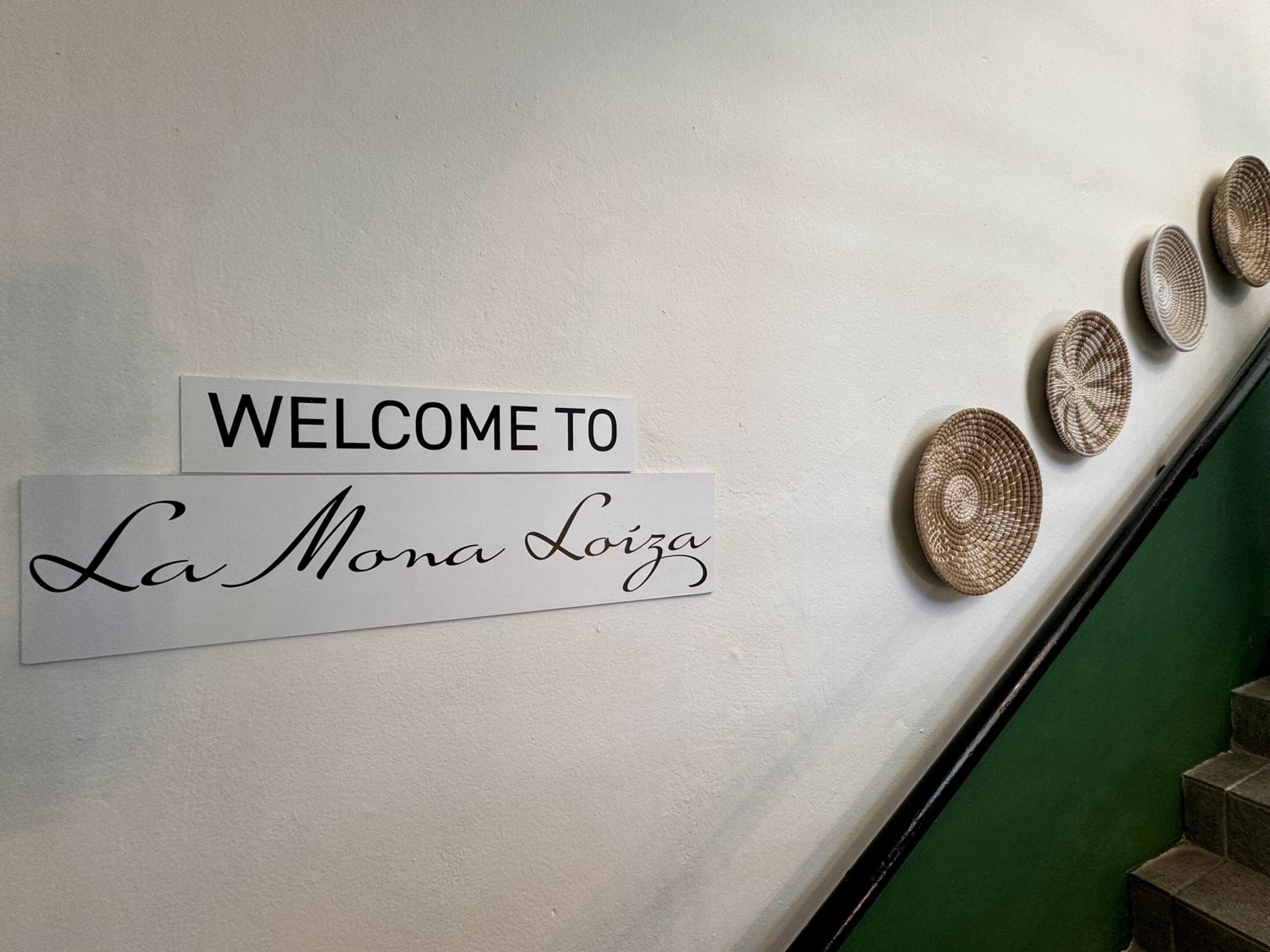 A welcome sign with "WELCOME TO La Mona Loiza" on a wall.