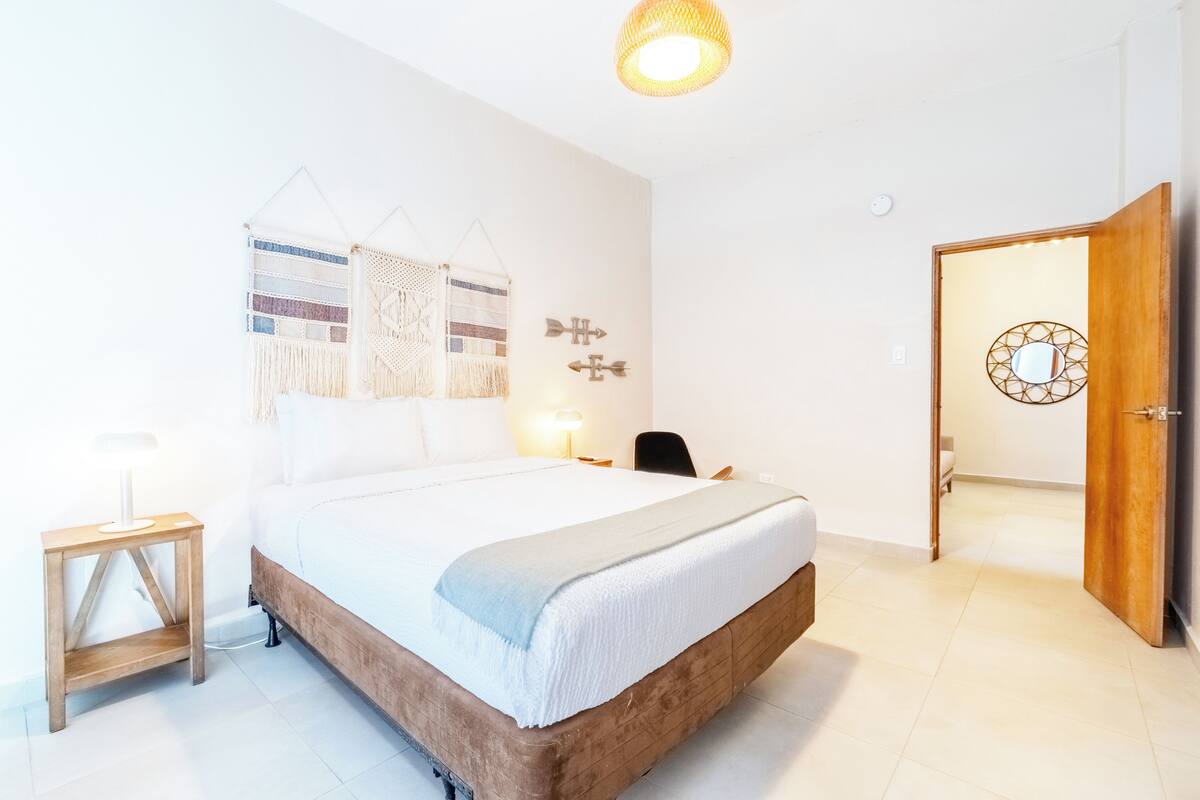 A bedroom with a bed, bedside table, lamp, wall art, and a door.