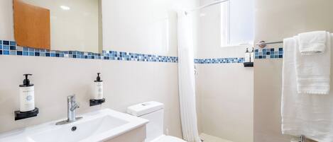 A bathroom with a white sink, toilet, and shower. There are two bottles of hand soap on the sink.