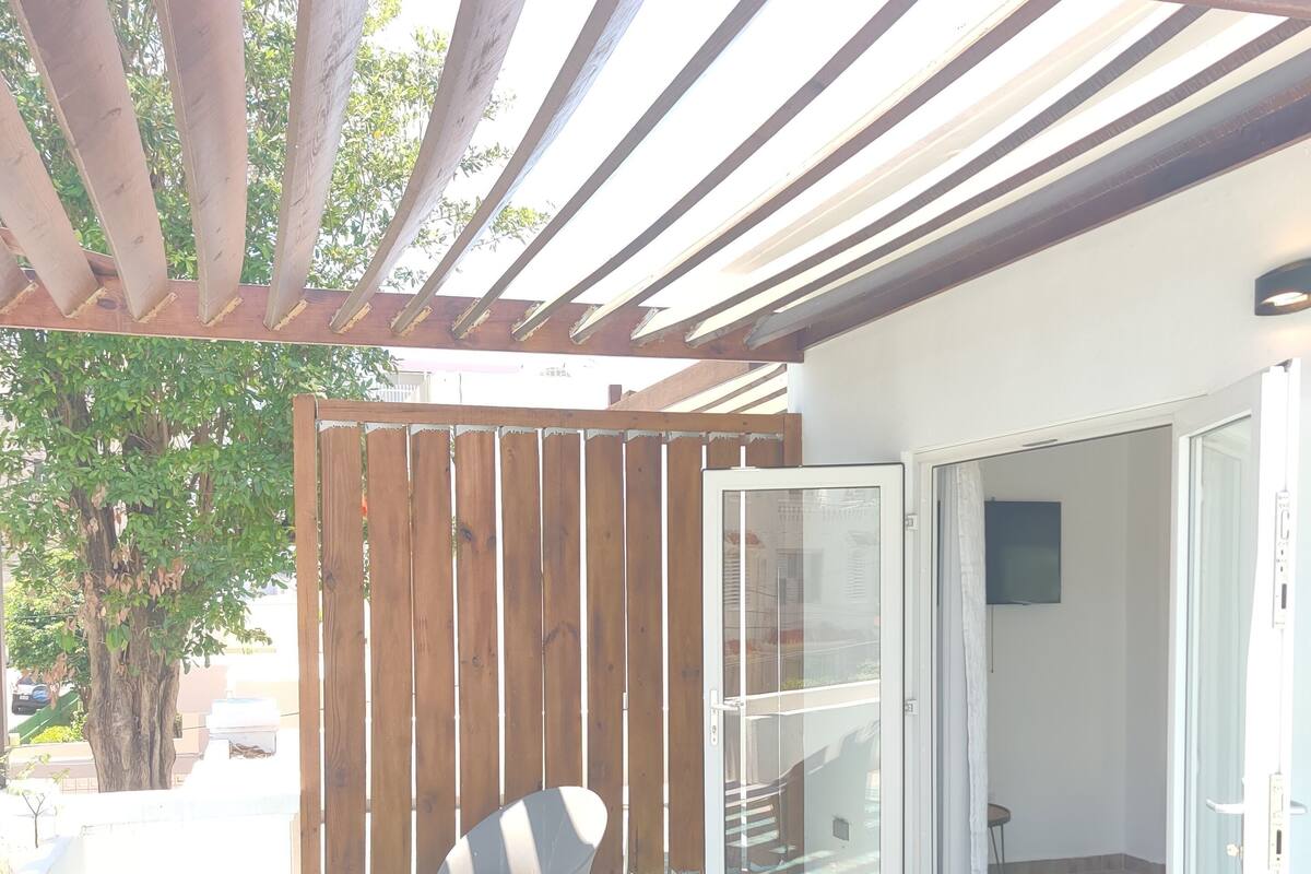 A covered patio with a tiled floor, a wooden fence, and a sliding glass door leading to an interior space.