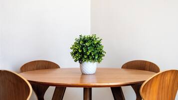 A round wooden table with a white pot of green plants in the center, surrounded by four wooden chairs.