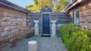 A wooden house with a dark door, two stone statues, and a gravel pathway. - Sophisticated Artist's Retreat (Stinson Beach)
