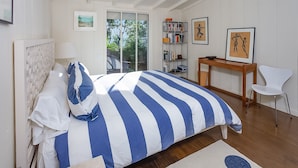 A bedroom with a large bed, a wooden desk, a white chair, and a bookshelf. - Sophisticated Artist's Retreat (Stinson Beach)