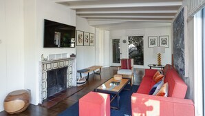 A living room with a fireplace, a sofa, a coffee table, and a television mounted on the wall. - Sophisticated Artist's Retreat (Stinson Beach)