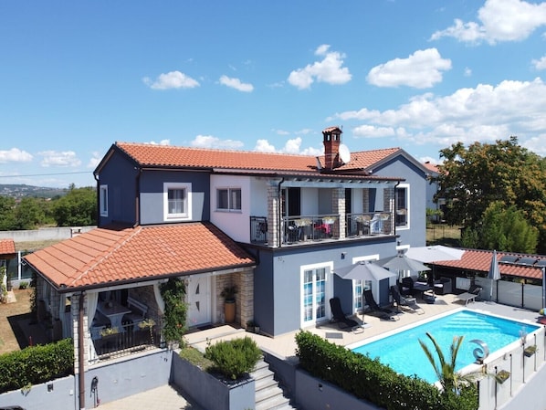 Une maison à deux étages dotée d’une piscine, d’un balcon aménagé avec du mobilier d’extérieur et offrant une vue sur le paysage environnant.