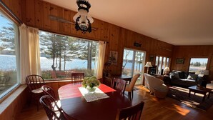Una cabaña de madera con comedor, sala de estar y ventanas amplias con vista al lago.