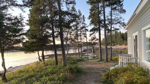 Un camino que lleva a una casa junto a un lago, rodeada de árboles y arbustos.