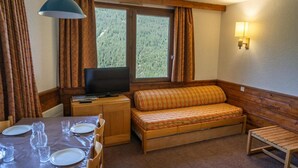 Ein gemütliches Zimmer mit einer hölzernen Bank, einem Fernseher und einem für zwei Personen gedeckten Esstisch.
