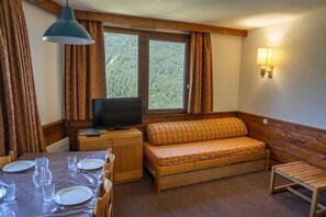 A cozy room with a wooden bench, a television, and a dining table set for two. - 100m from resort center, 10th floor, view mountain, balcony, tv, ski locker, 39m², Les Orres (Les Orres)