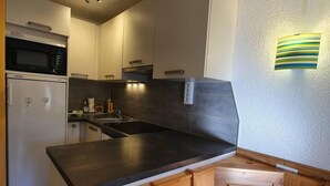 Una cocina moderna con encimera negra, armarios de madera, microondas integrado y un lavamanos.