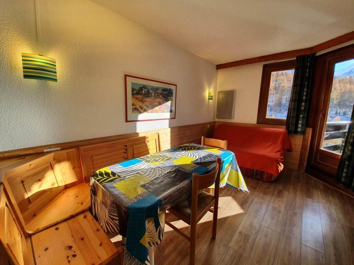 A dining area with a wooden table and benches, a painting on the wall, and a view of a snowy landscape through a window.