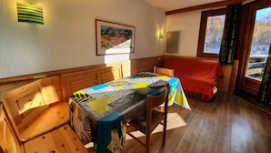 Un comedor con una mesa y bancos de madera, un cuadro en la pared y vistas a un paisaje nevado a través de una ventana.