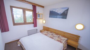 A bedroom with a wooden bed, a window with curtains, a wall-mounted cabinet, and a painting of a mountain landscape. - 100m from ski slopes, 10th floor, balcony, tv, ski locker, 45m², Les Orres (Les Orres)