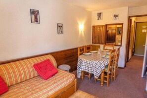 A cozy room with a sofa, a dining table set for four, and a small stool. - 100m from resort center, 10th floor, balcony, tv, ski locker, 30m², Les Orres (Les Orres)