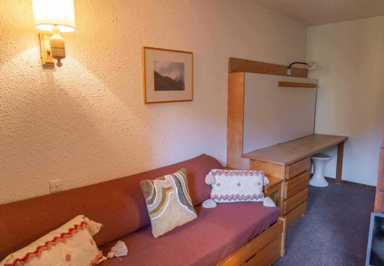 Ett mysigt rum med en träbänk, en bekväm soffa med mönstrade kuddar och en väggmonterad lampa.