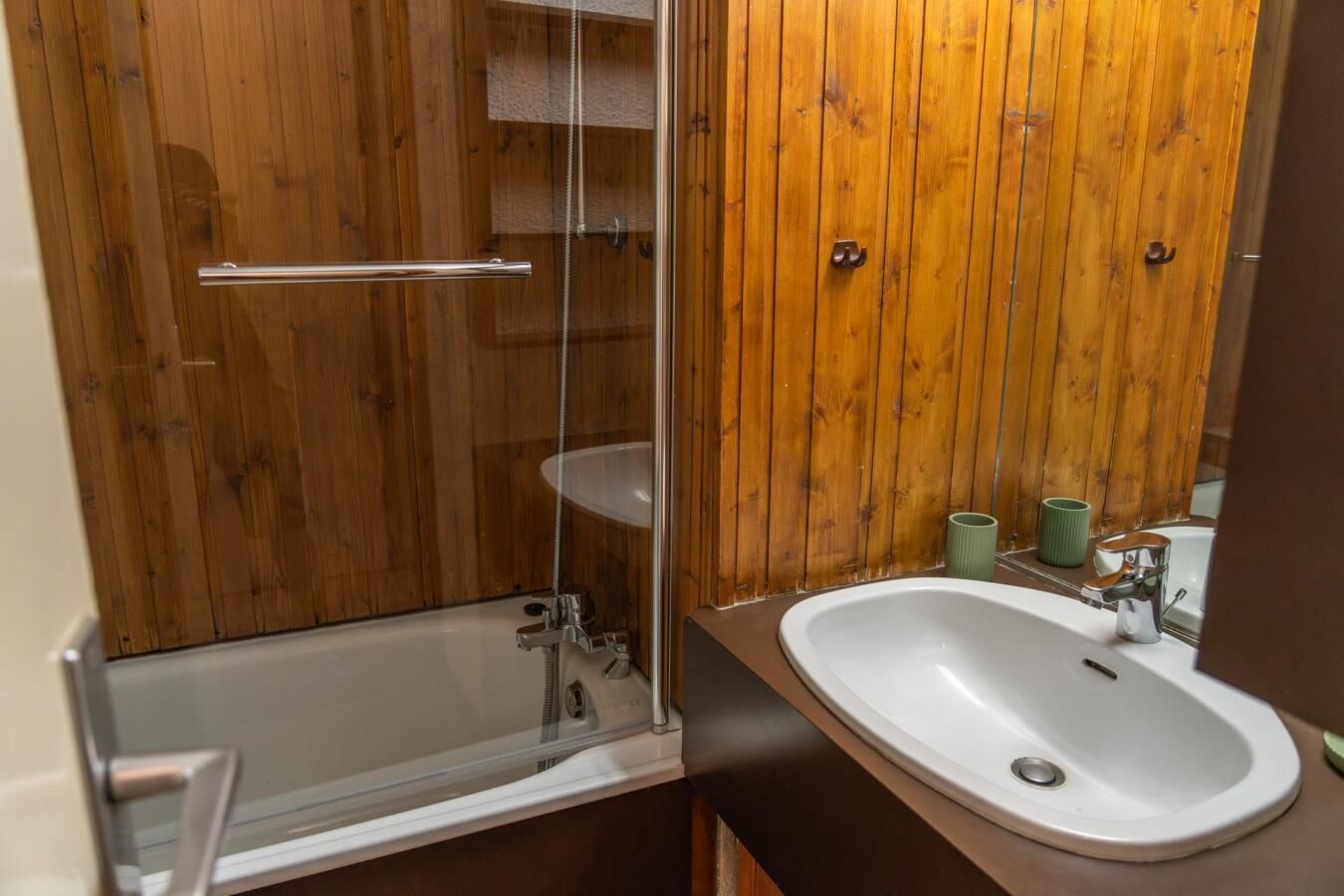 A bathroom with a glass-enclosed shower, a white sink, and wooden paneling.