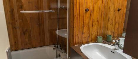 A bathroom with a glass-enclosed shower, a white sink, and wooden paneling.
