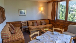A cozy room with a sofa, chairs, a dining table set for two, and a window with a view of trees and mountains. - 100m from ski slopes, 3rd floor, balcony, tv, ski locker, 39m², Les Orres (Les Orres)
