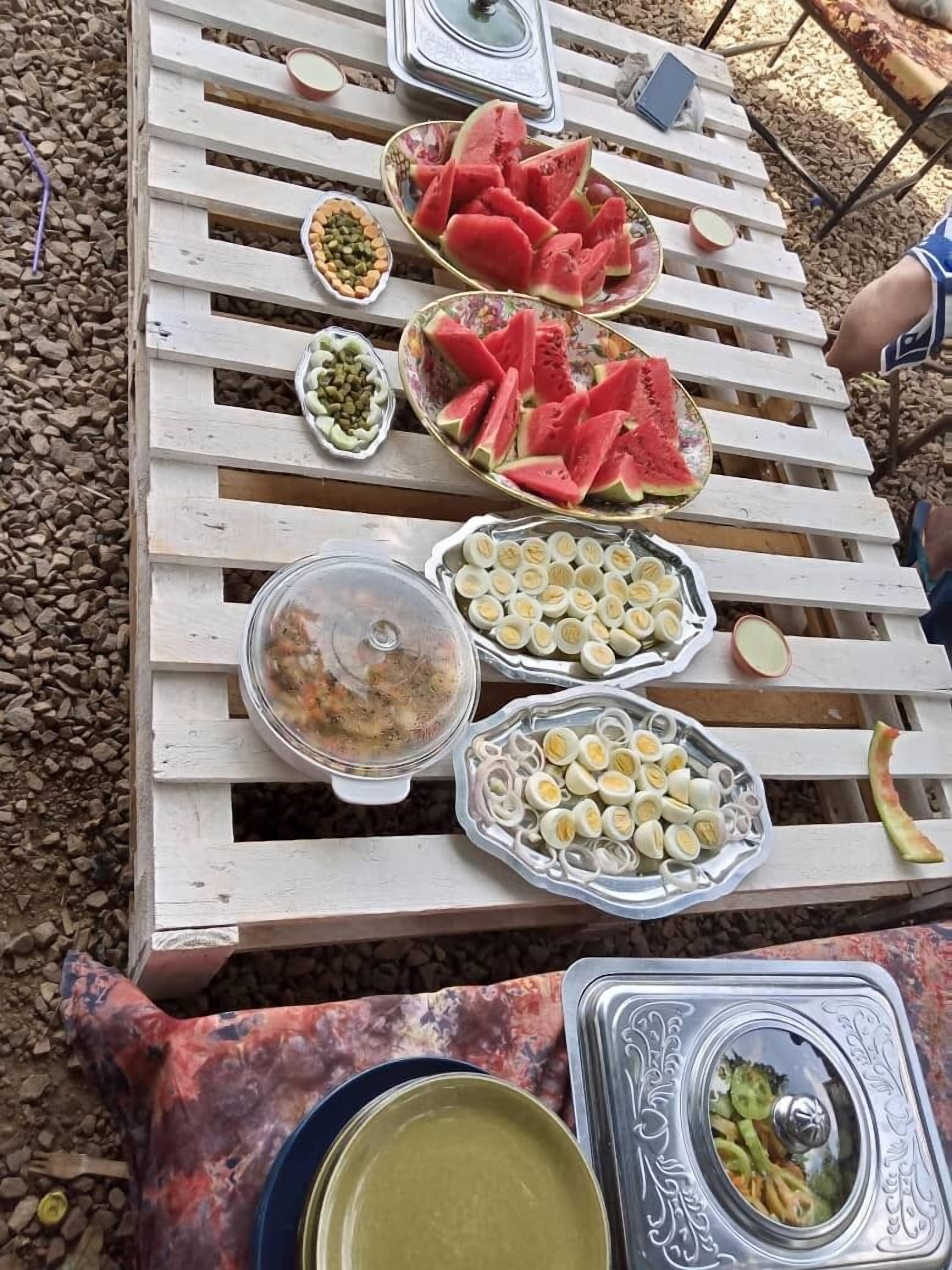Une table en bois sur laquelle on trouve divers aliments, notamment de la pastèque, des œufs et une salade.