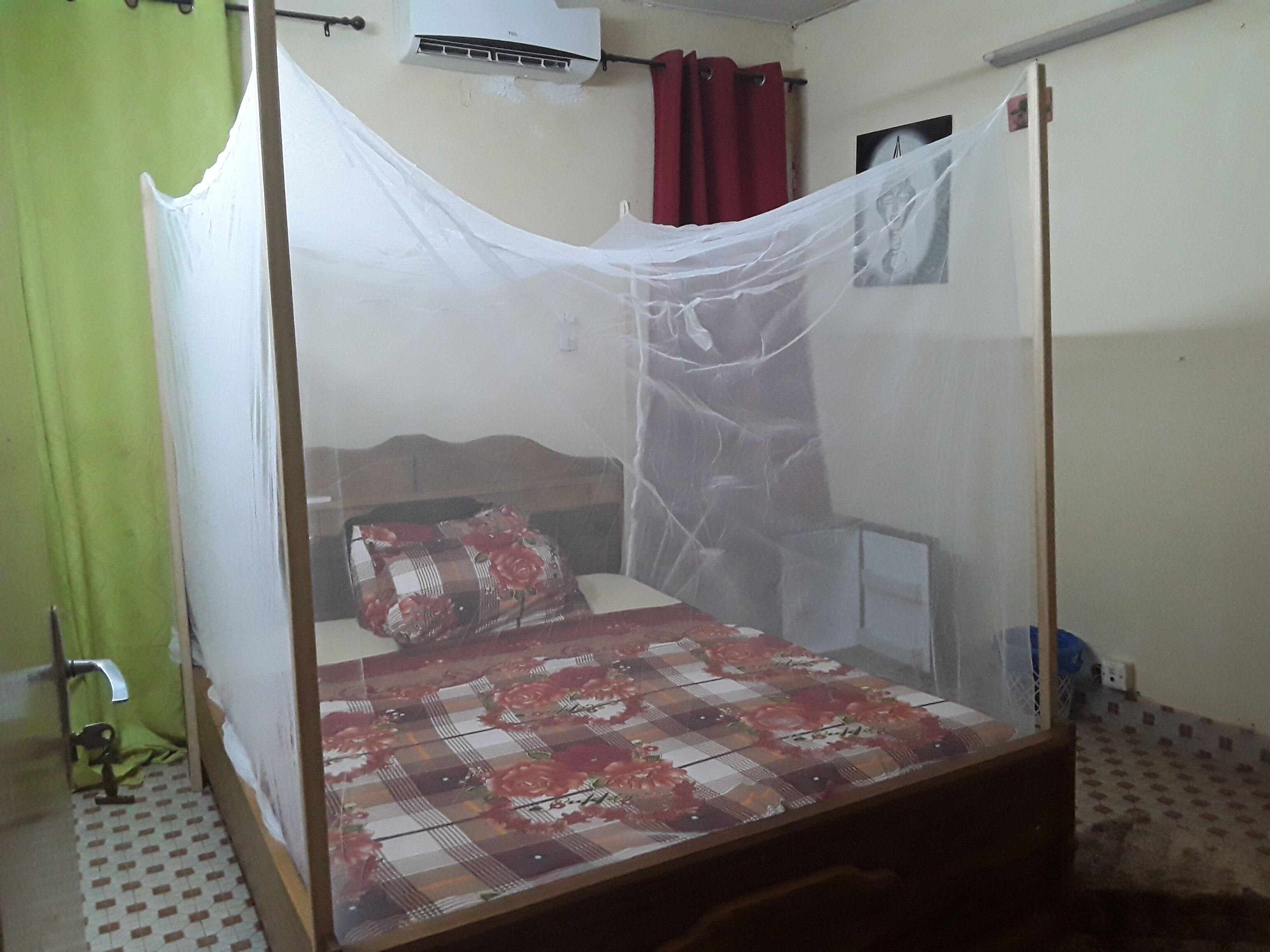 A single bed with a mosquito net, a red curtain, and a wall-mounted air conditioner.