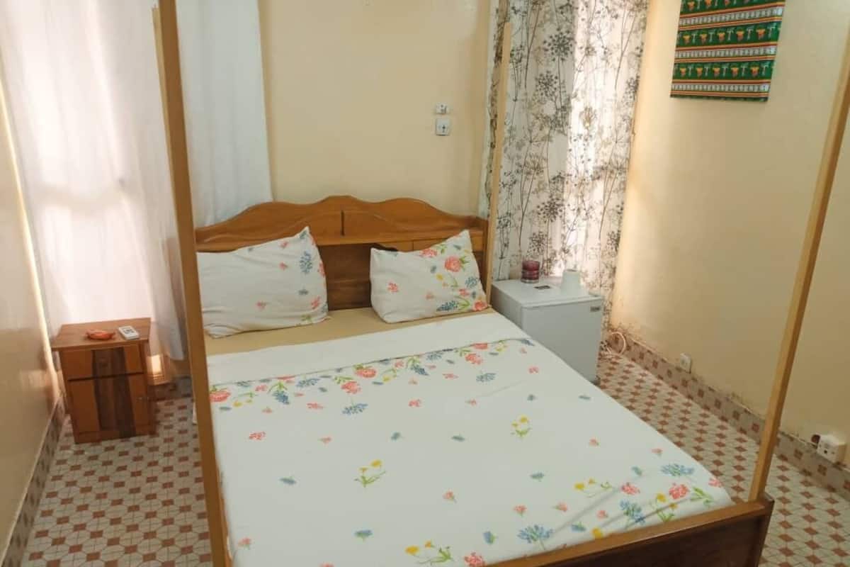 A bedroom with a wooden bed, floral bedding, a nightstand, a small cabinet, and a patterned curtain.