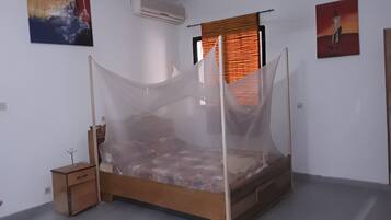 A bedroom with a wooden bed, a nightstand, a wall-mounted air conditioner, and two paintings.