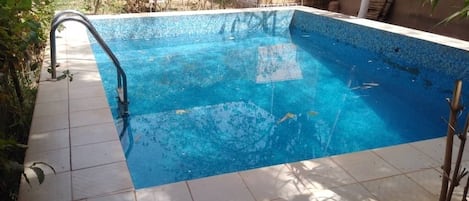 Ein rechteckiger Pool mit Fliesenrand, umgeben von Bepflanzung und einem Gebäude im Hintergrund.