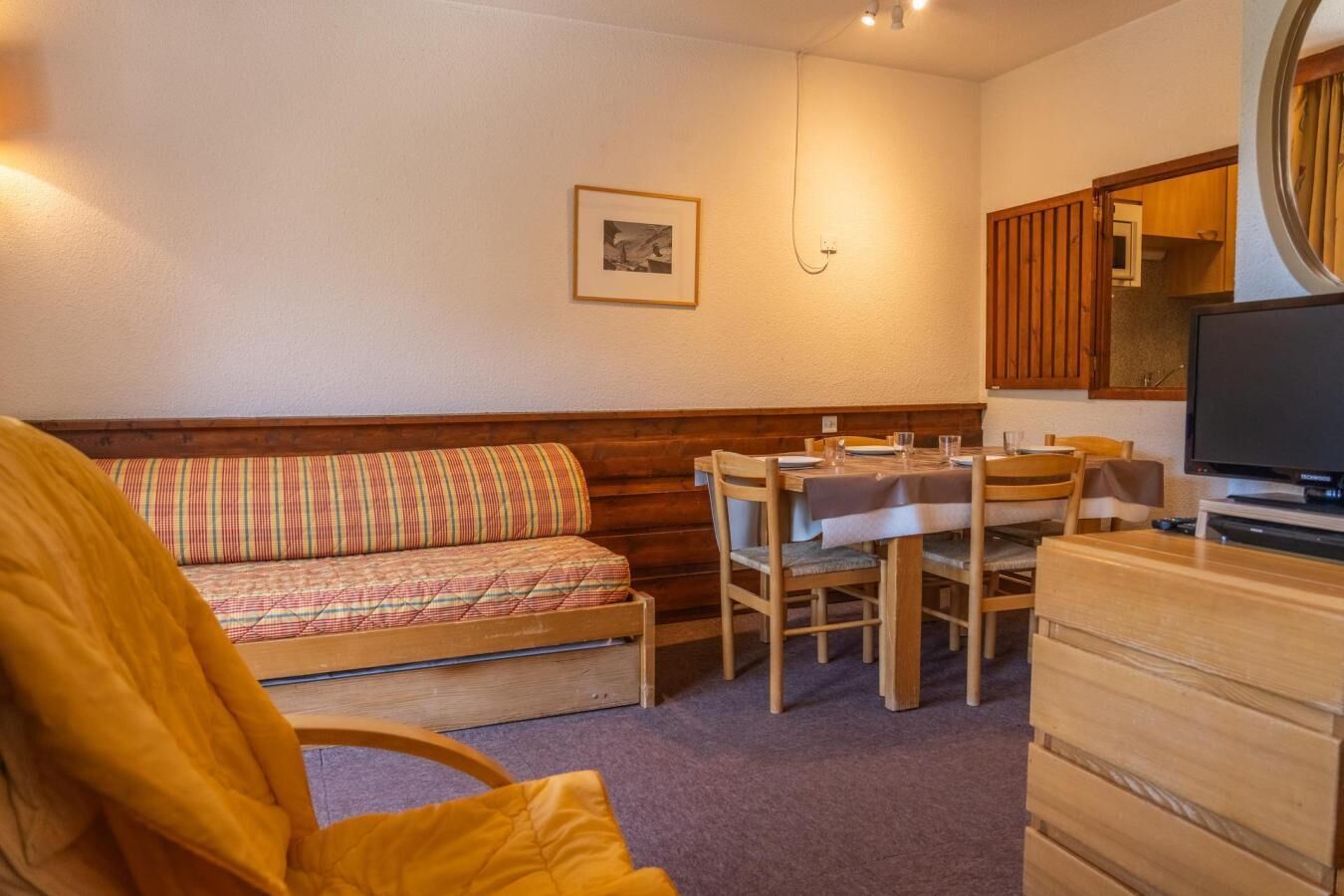 A cozy room with a wooden bench, a dining table with chairs, a television, and a small cabinet.