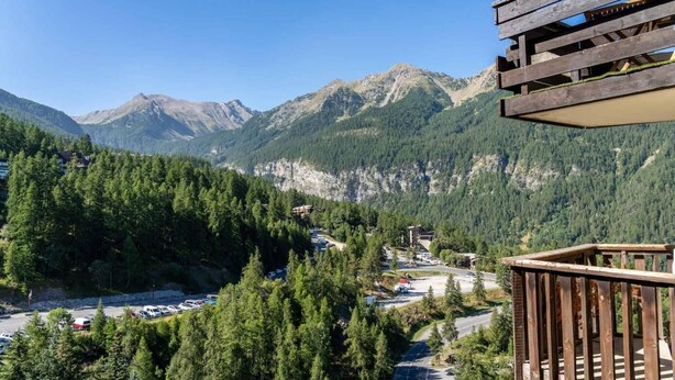 A mountain view with a wooden deck overlooking a parking area and buildings. - 100m from ski slopes, 10th floor, view mountain, balcony, tv, ski locker, 31m², Les Orres (Les Orres)