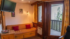 Una habitación acogedora con un sofá de madera, un televisor montado en la pared y un ventanal con vistas a árboles.