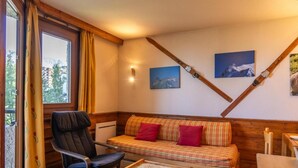 Una habitación acogedora con sofá, sillón, mesita y ventana con cortinas.