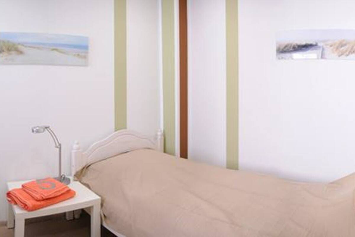 A single-bed room with a bedside table, a lamp, and a cabinet.