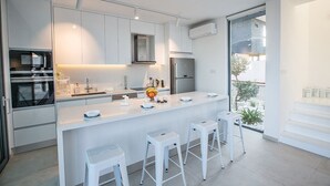 A modern kitchen with white cabinetry, stainless steel appliances, and a central island with bar stools. - Villa Charlize, Luxury and Contemporary 3BDR Kapparis Villa with Private Pool (Protaras)
