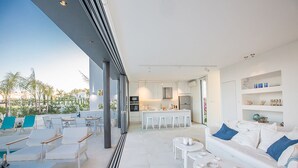 A modern living area with a pool, white furniture, and a kitchen in the background. - Villa Charlize, Luxury and Contemporary 3BDR Kapparis Villa with Private Pool (Protaras)